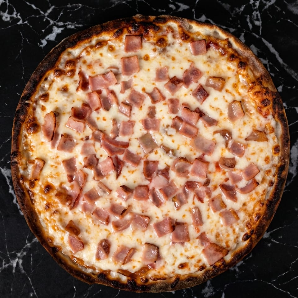 Pizza de jamón con queso fundido y borde dorado sobre mármol negro.