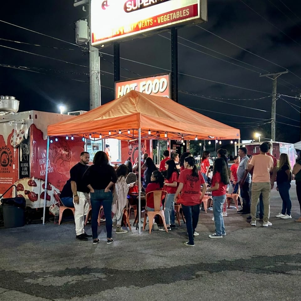Personas reunidas junto a un camión de tacos iluminado bajo un toldo naranja por la noche.