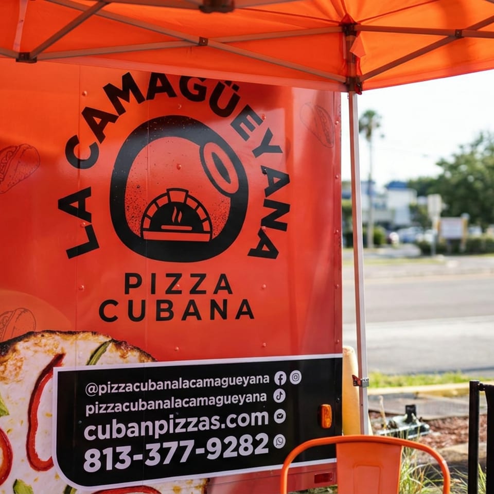 Remolque naranja de La Camagüeyana Pizza Cubana con logotipo, imagen de pizza, sitio web y teléfono.