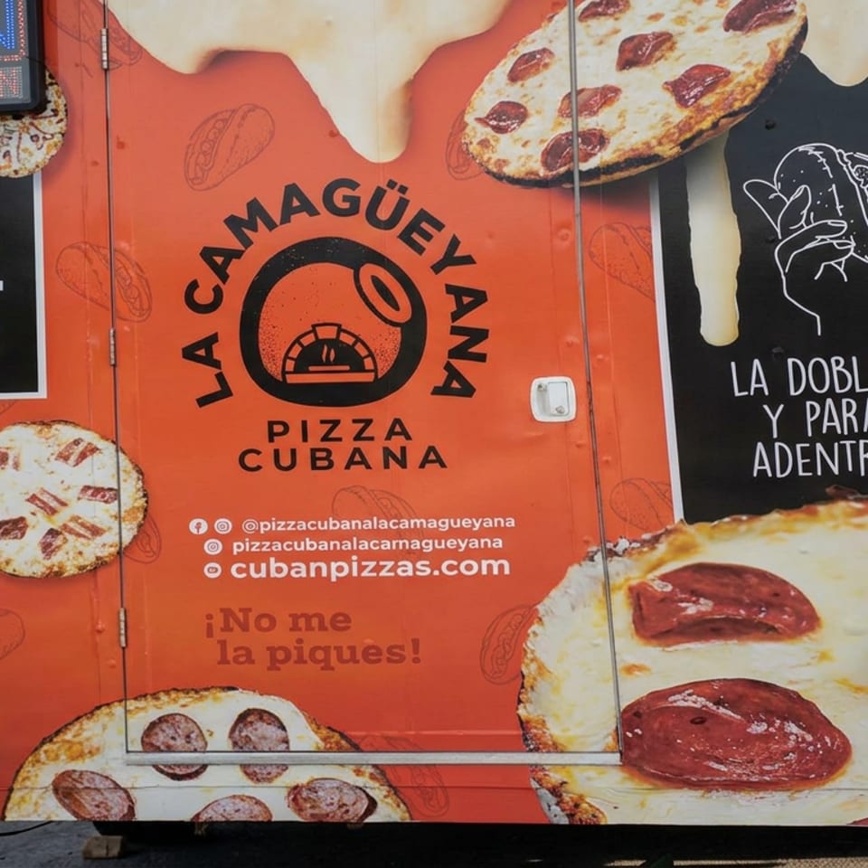 Camión naranja de pizza cubana La Camagüeyana con imágenes grandes de pizzas de pepperoni y letrero de abierto.
